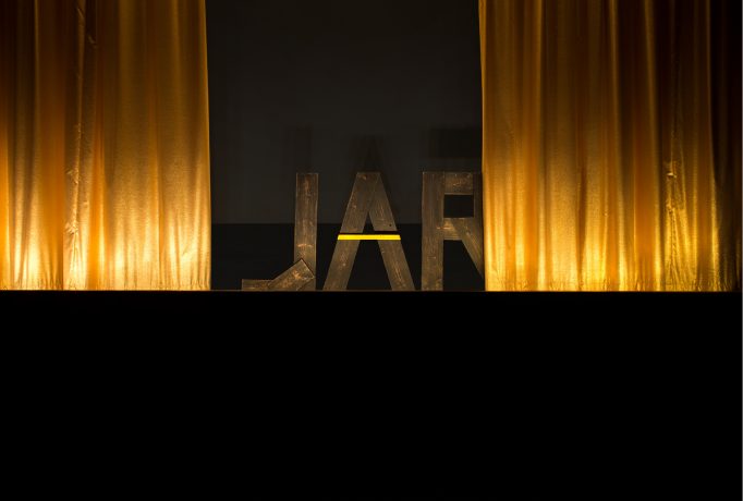 letters ‘JAR’ made out of wood standing in the back between two golden curtain