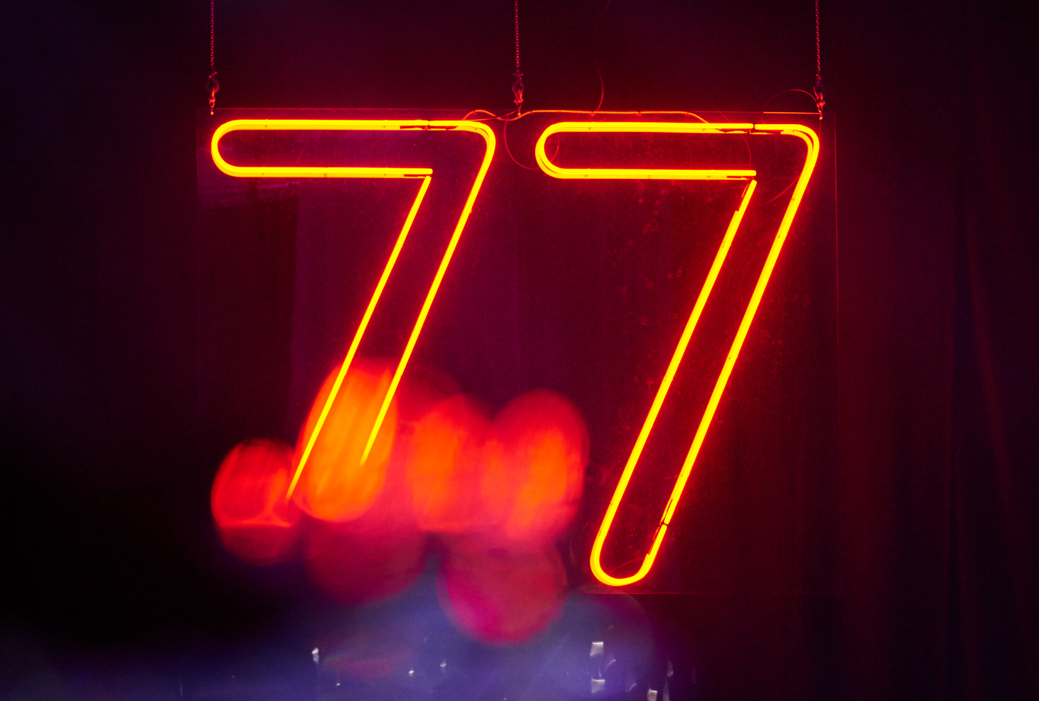 orange neon lights forming the number 77 on a dark blue background with some red light spots