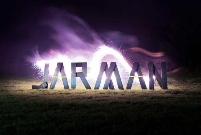 word ‘JARMAN’ made out of wooden letters standing on grass, in front of bright flair