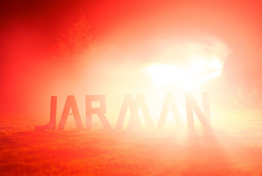 word ‘JARMAN’ made out of wooden letters standing on grass, illuminated by a red smoke flair