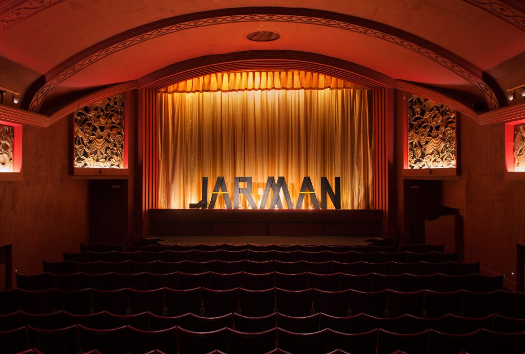 old cinema with red walls, word ‘JARMAN’ made out of wooden letters standing on the stage