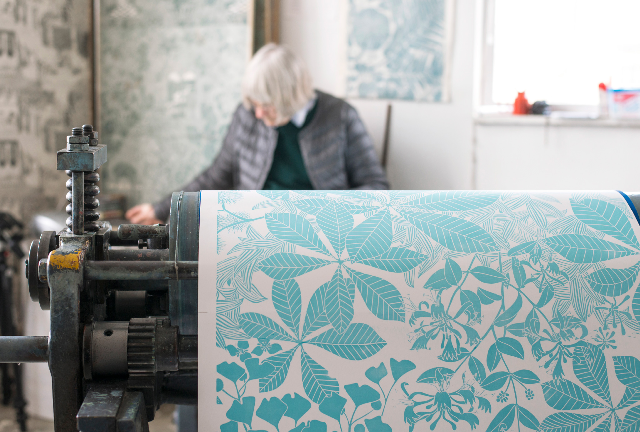 Marthe’s studio with her in the background, some fabric designs on the wall and a hand printed design in the front