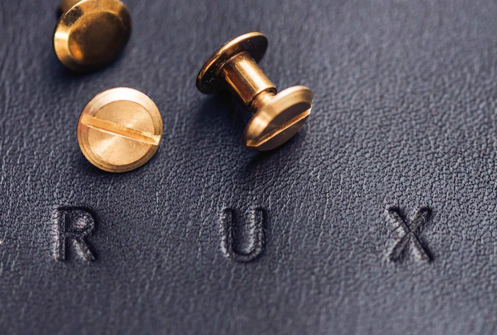 ‘RUX’ blind embossed into black leather and three golden screw nearby