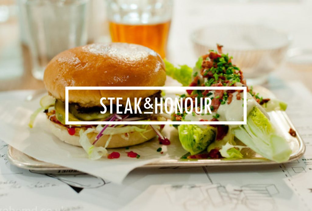 burger and salad on a plate with white ‘STEAK & HONOUR’ written block in front