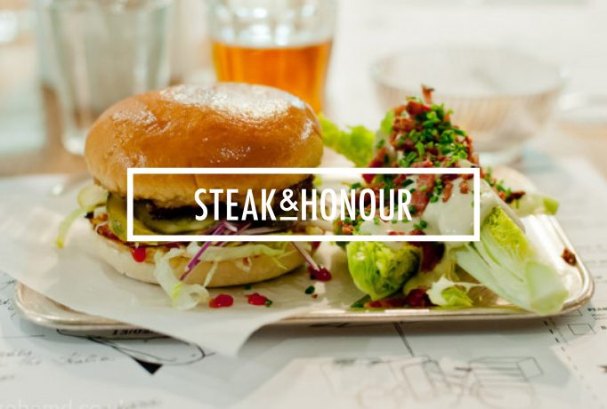 burger and salad on a plate with white ‘STEAK & HONOUR’ written block in front